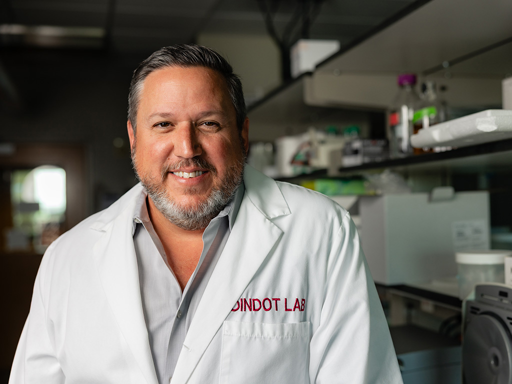 A researcher in a white coat with a laboratory in the background.