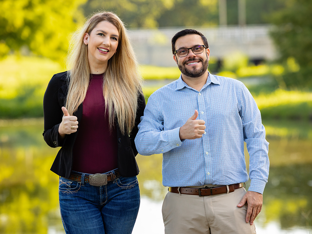 Two researchers standing outdoors giving the gig 'em gesture.