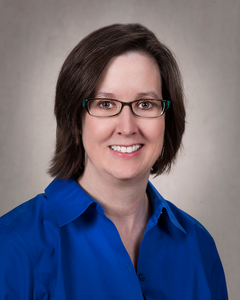 A university headshot of a woman with glasses in a blue shirt.