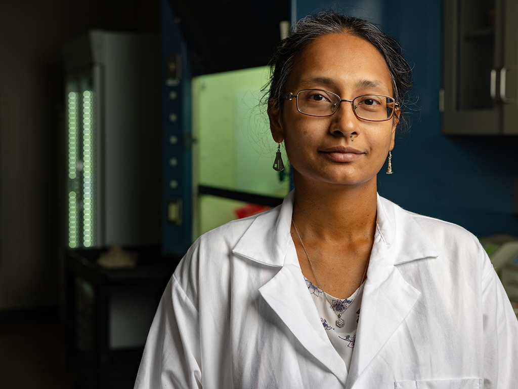 A female researcher in a white lab coat stands in her laboratory.