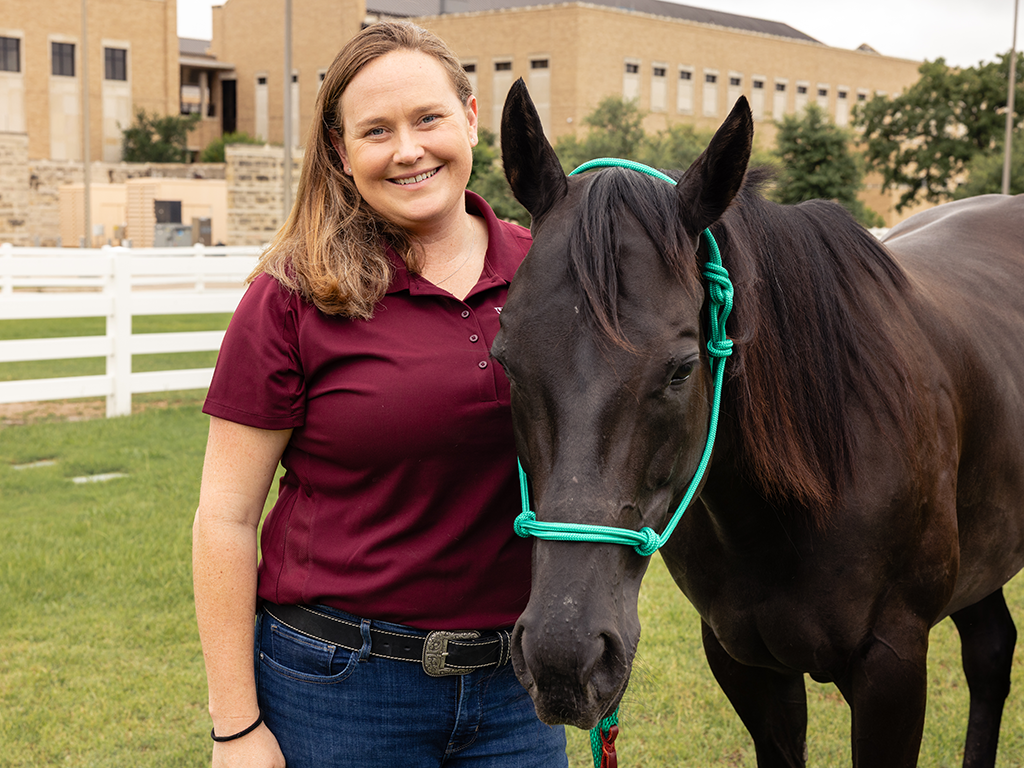 A woman in a maroon shirt standing beside a black horse