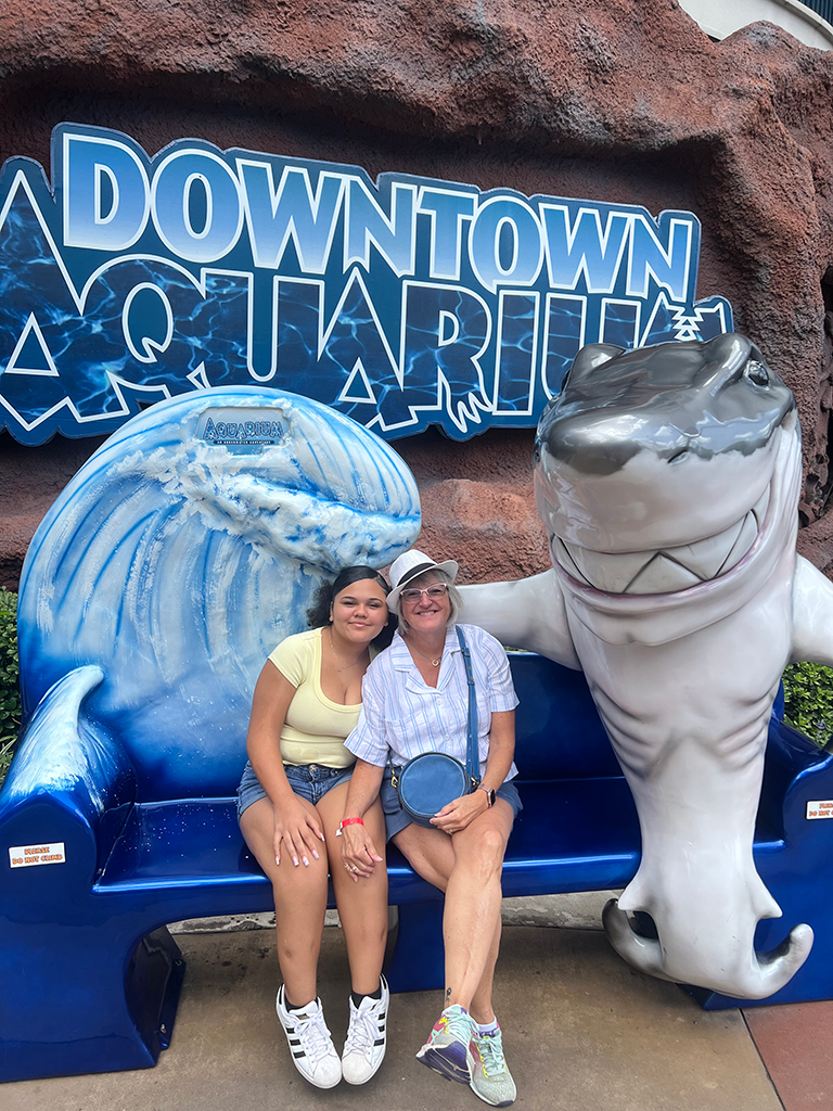 Two women sit on a bench outside an aquarium.