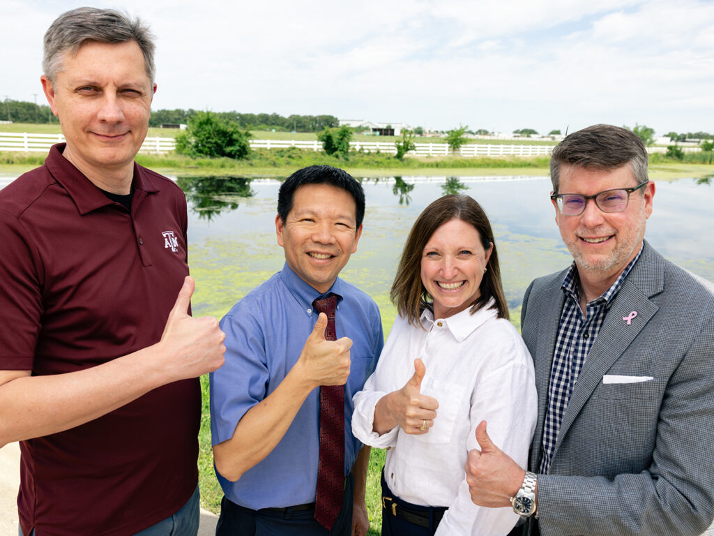 Four researchers standing in front of a pond doing gig 'em