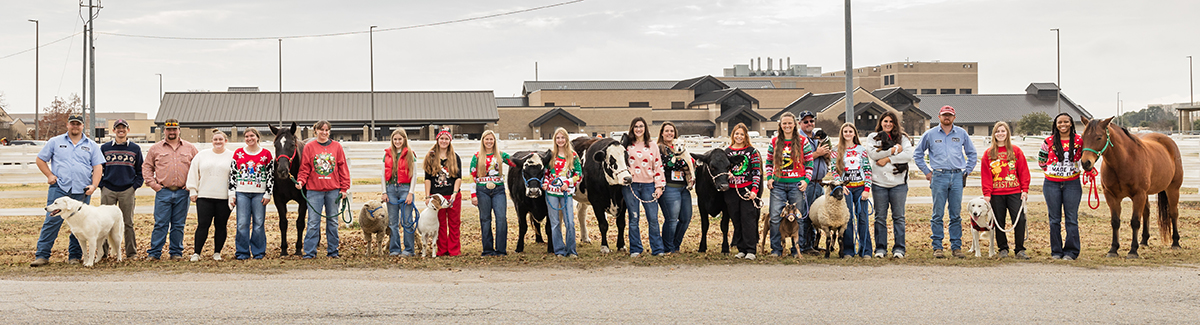 Group of people posing in front of building with various animals in holiday attire
